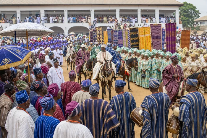 Colourfully dressed Ijebu age-grade groups and horse riders gathered respectfully near a palace forecourt during a heritage festival.