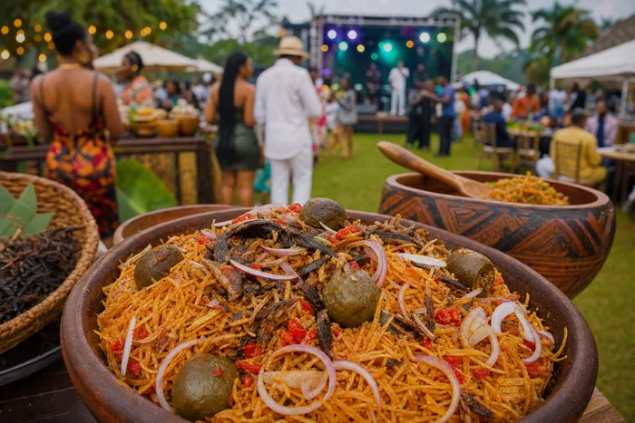 Close-up of prepared abacha with vendors, music stage lights and a relaxed Port Harcourt outdoor festival crowd in the background.