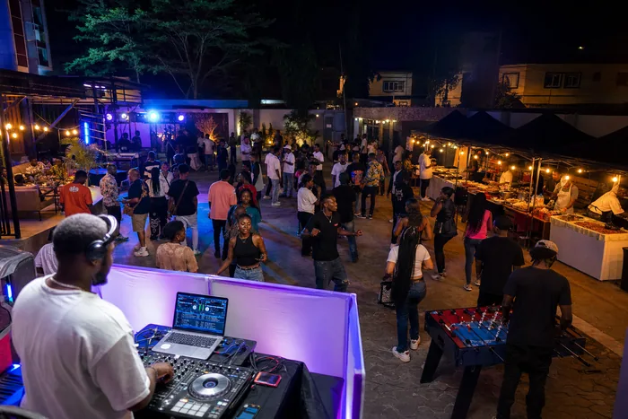 A Lagos mainland night party scene with DJ lights, young people in streetwear, food stalls and a hotel event courtyard atmosphere.