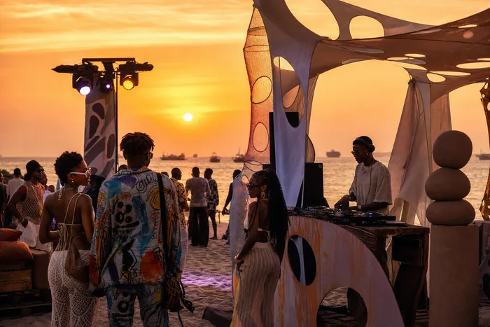 A sunset beach music event in Lagos with a DJ booth, stage lights, art installations and young adults gathered near the shoreline.
